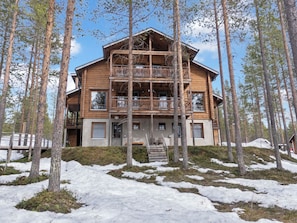 Een houten vakantiehuis met meerdere verdiepingen en een balkon, omgeven door bomen en sneeuw.