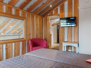Een kamer met een bed, een rode stoel, een aan de muur bevestigde televisie en houten lambrisering.