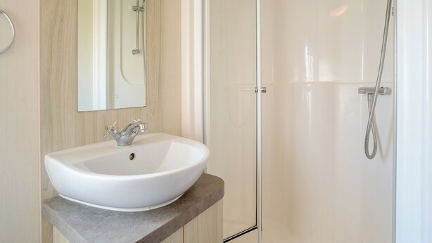 Un baño con lavamanos blanco, un espejo y cabina de ducha con mampara de vidrio.