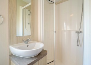 Un baño con lavamanos blanco, un espejo y cabina de ducha con mampara de vidrio.