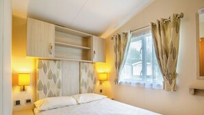 Un dormitorio con una cama, dos lámparas de pared, un ventanal con cortinas y un armario empotrado.