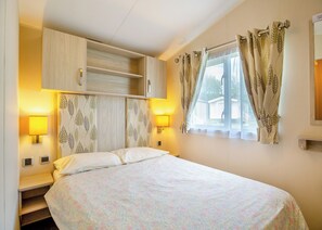 Un dormitorio con una cama, dos lámparas de pared, un ventanal con cortinas y un armario empotrado.