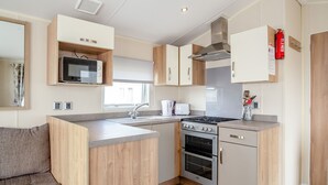 Una cocina compacta con microondas, estufa y horno integrados, muebles de madera y un ventanal que proporciona luz natural.