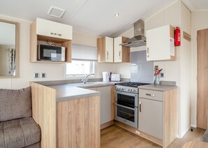 Een functionele keuken met een ingebouwde magnetron, kookplaat en oven, houten keukenkastjes en een raam voor natuurlijk licht.