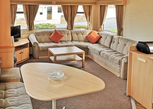 A cozy RV interior with a sectional sofa, a small table, a TV, and a cabinet.