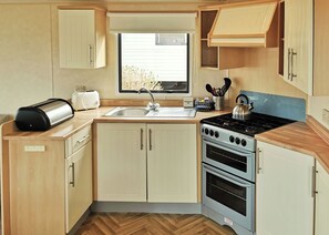 A compact kitchen with a sink, a toaster, a kettle, and a stove. - Spacious and comfortable 12ft-wide caravan with one double and two twin. (Cross Inn, Nr New Quay)