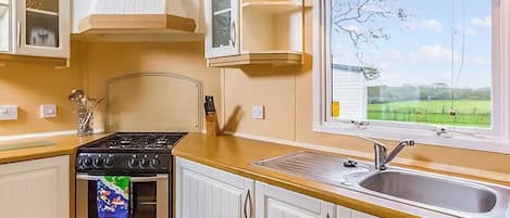 Une cuisine équipée d’une cuisinière, d’un four, d’un évier et d’une fenêtre donnant sur un paysage verdoyant.