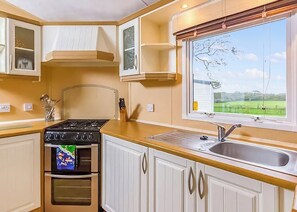 A kitchen with a stove, oven, sink, and window with a view of a green landscape.