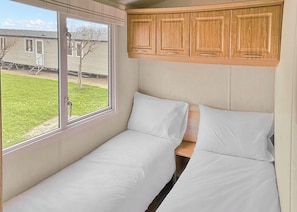 A single bed with white bedding, a window with a view of a house and lawn, and wooden cabinets above the bed. - 3 bedroom accommodation in Newbridge, Nr Yarmouth (Newbridge, Nr Yarmouth)