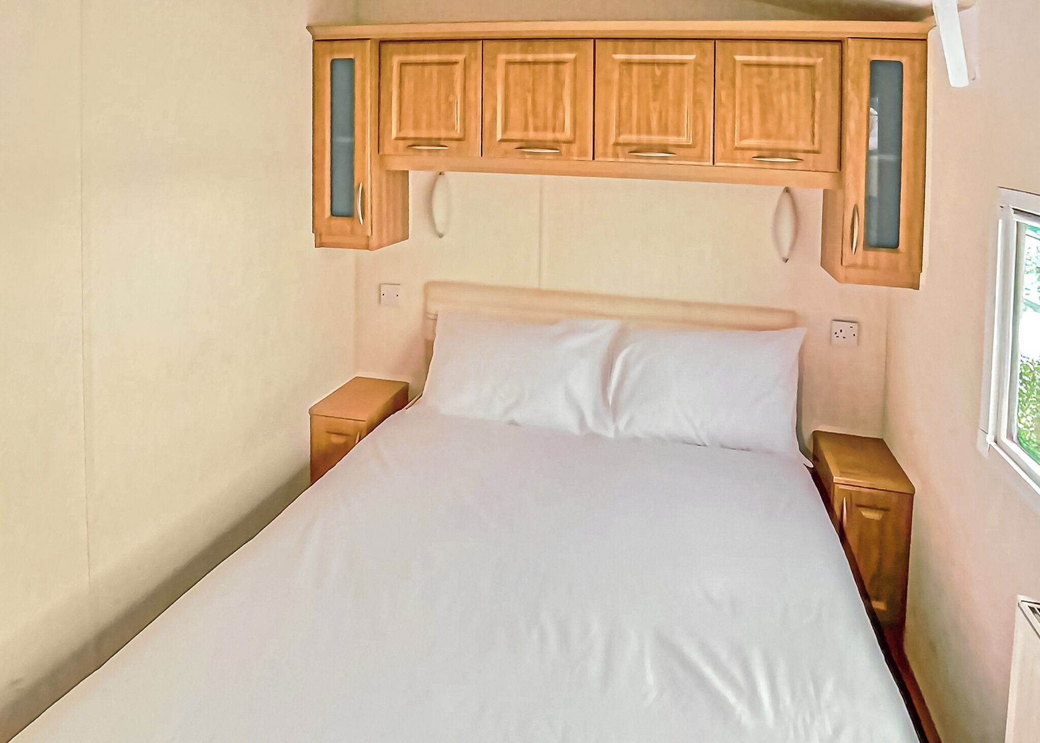 Ein Schlafzimmer mit einem Bett, Holzschränken darüber und einem Fenster auf der rechten Seite.