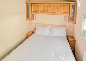 A bedroom with a bed, wooden cabinets above the bed, and a window on the right.
