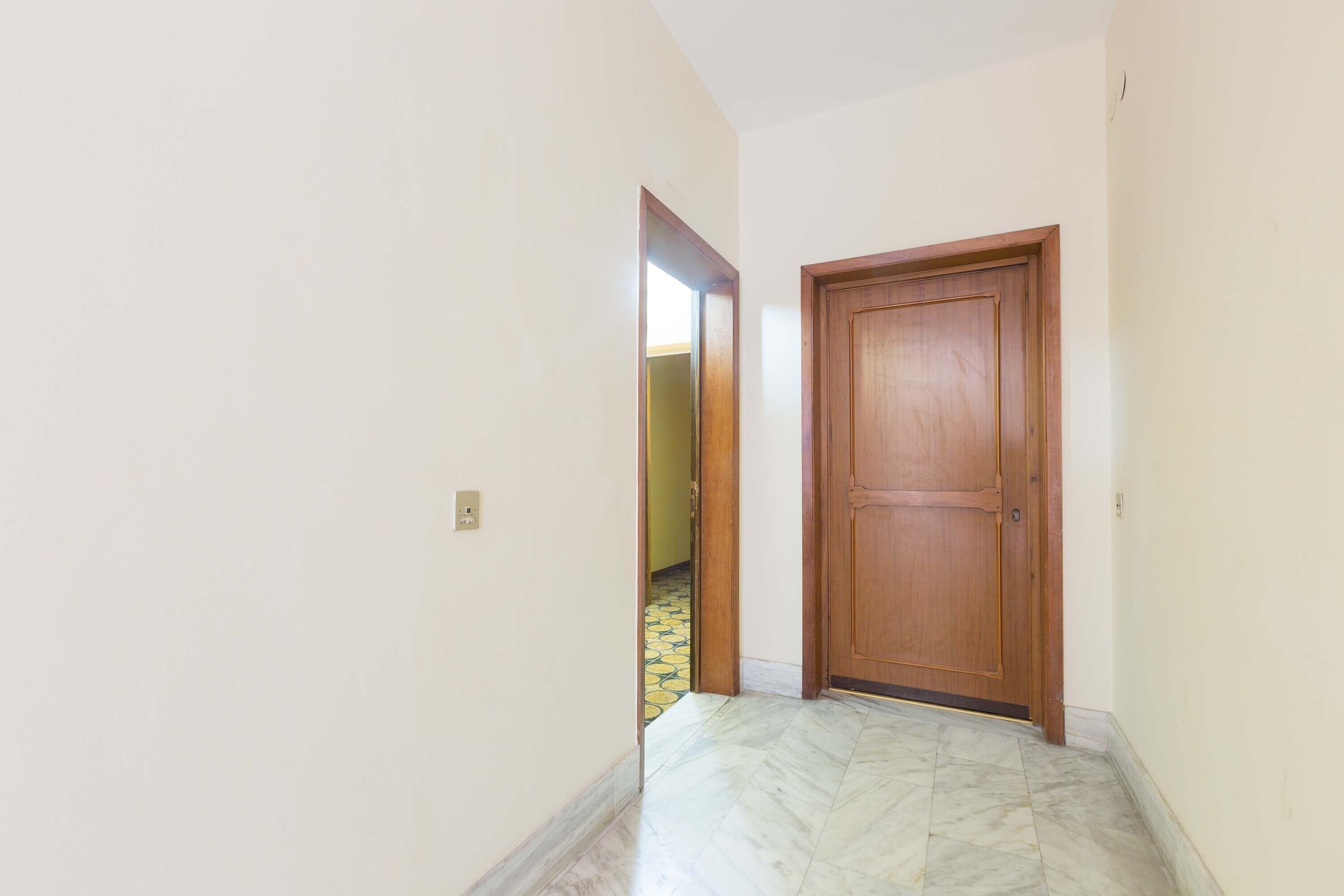 Un couloir avec une porte en bois et un sol en marbre.