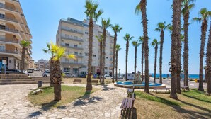 A paved walkway lined with palm trees and benches, leading to a pool area with a blue circular design. - 3040 Appartamento Bludamare by Barbarhouse (Gallipoli)