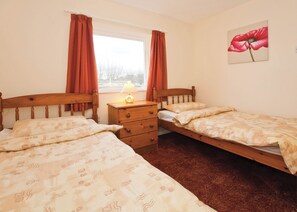 A bedroom with two single beds, a wooden dresser, a window with curtains, and a painting of a flower on the wall.