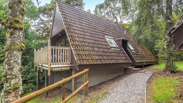 A house with a sloped roof, a balcony, and a gravel driveway. - Highland Ranch Lodge (Delny, Nr Invergordon)
