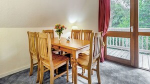 A dining area with a wooden table and chairs, a vase with flowers, and a view through a glass door. - Highland Ranch Lodge (Delny, Nr Invergordon)