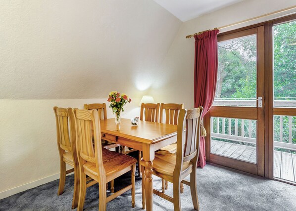 Ein Essbereich mit Holztisch und Stühlen, einer Vase mit Blumen und Blick durch eine Glastür.
