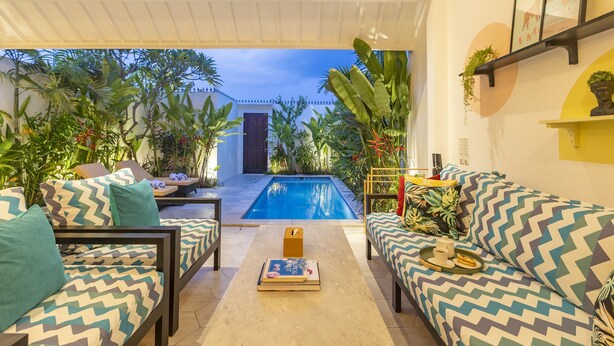 A poolside area with a sofa set, a coffee table, and a view of the pool and house. - Villa Caorrun (Canggu)