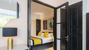 A hotel room with a bed, a bedside table with a lamp, and a door leading to another room. - Villa Caorrun (Canggu)