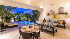 A poolside area with a dining setup, lounge chairs, and a sofa. - Villa Caorrun (Canggu)