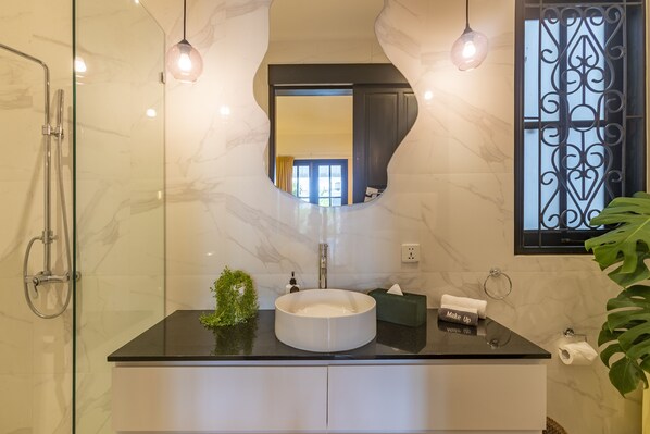 Un baño moderno con ducha envuelta en vidrio, un lavabo redondo e iluminación colgante.