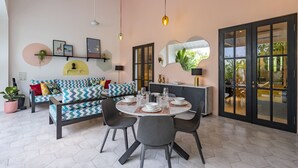 A modern living room with a round dining table, grey chairs, a sofa with patterned cushions, and a large mirror. - Villa Caorrun (Canggu)