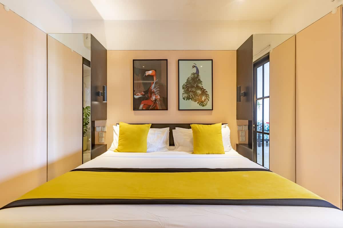 Una habitación de hotel moderna con una cama grande, ropa de cama amarilla y dos cuadros en la pared.