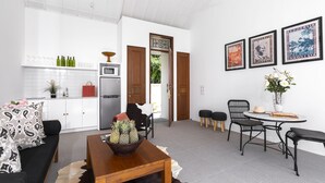 A modern living room with a sofa, coffee table, and chairs. A kitchen with white cabinets and a refrigerator is visible in the background. - Villa Anahera (Seminyak)