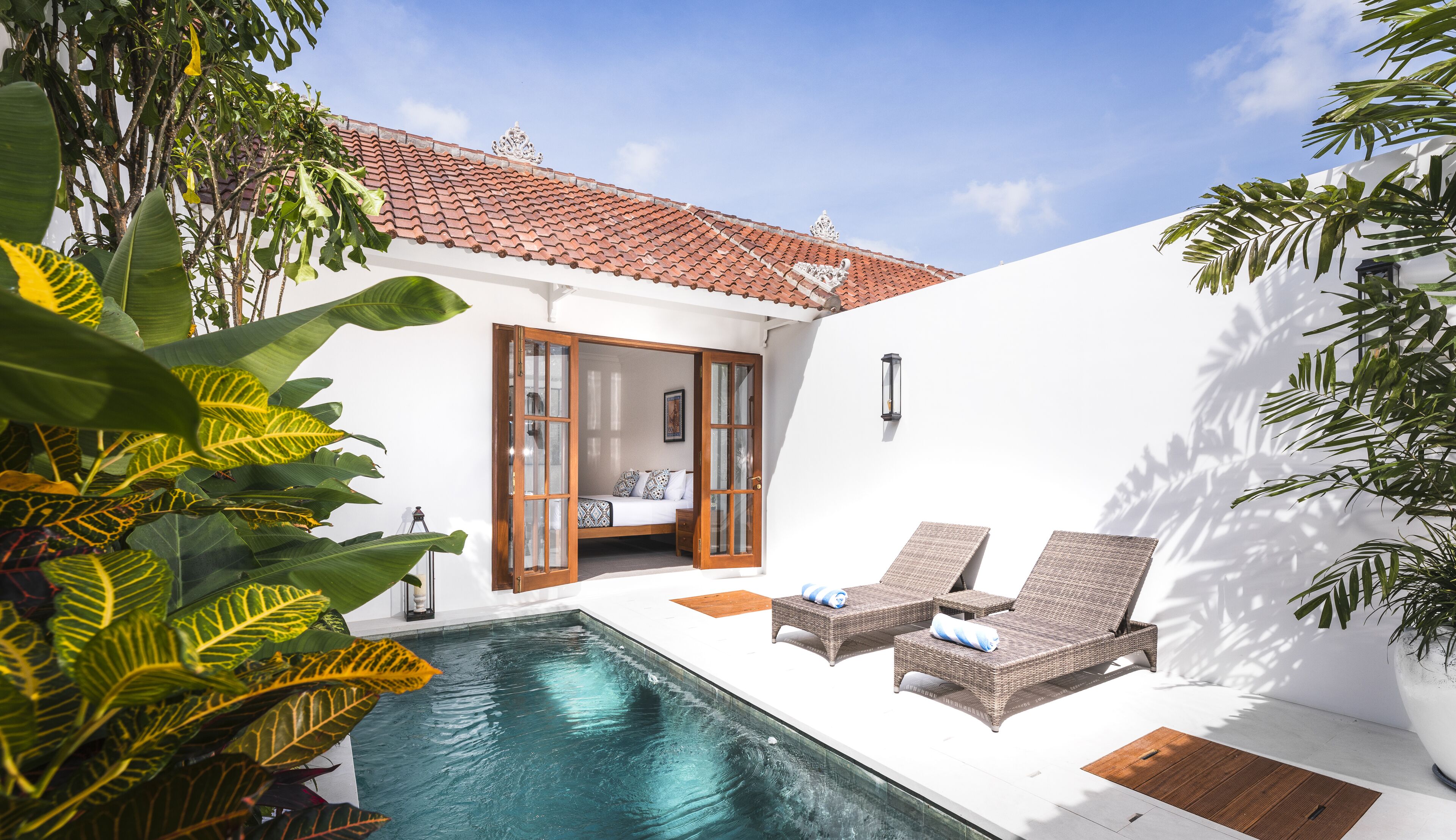 A private pool area with a bed and lounge chairs, surrounded by tropical plants.