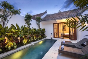 Un espace aménagé au bord de la piscine, doté d’un toit en carrelage, d’une chaise longue et d’un jardin bien entretenu où poussent différentes espèces de plantes.