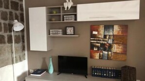 A living room with a flat-screen TV, a white cabinet, a shelf with books and decorative items, and a large abstract painting on the wall. - San Faustino Guesthouse Domus Tuscia (Viterbo)