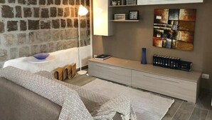 A modern living room with a stone wall, a sofa, a coffee table, a lamp, a bookshelf, and a decorative wall piece. - San Faustino Guesthouse Domus Tuscia (Viterbo)