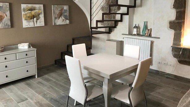 A dining area with a white table and chairs, a staircase, and artwork on the walls. - San Faustino Guesthouse Domus Tuscia (Viterbo)