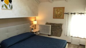 A bedroom with a bed, bedside table, lamp, radiator, and a painting on the wall. - San Faustino Guesthouse Domus Tuscia (Viterbo)