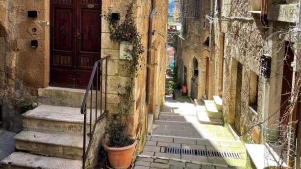Una estrecha calle empedrada de piedra, con una puerta de madera tradicional y escalones que conducen a un edificio.