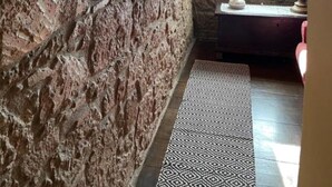 Una pared de piedra rústica con un estante que sostiene objetos decorativos y una ventana con luz natural.