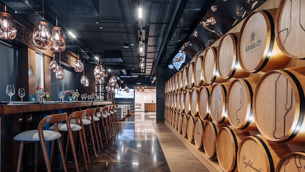 Zona de bar con barriles de madera, taburetes y lámparas colgantes.