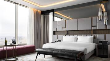Een moderne hotelkamer met een groot bed, een bankje, een nachtkastje en uitzicht op de stad.