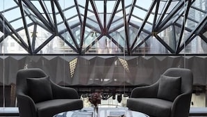 Un interior moderno con techo de vidrio, dos sillones, una mesa de centro de vidrio y vistas a la ciudad.