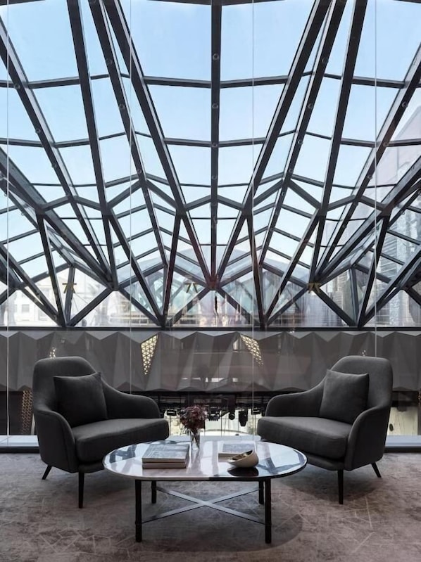 A modern interior with a glass ceiling, two armchairs, a glass coffee table, and a view of the cityscape.