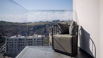 A balcony with a sofa and cushions, overlooking a cityscape and hills.