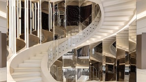 Una escalera espiral moderna con barandillas de vidrio reflectante y peldaños blancos.