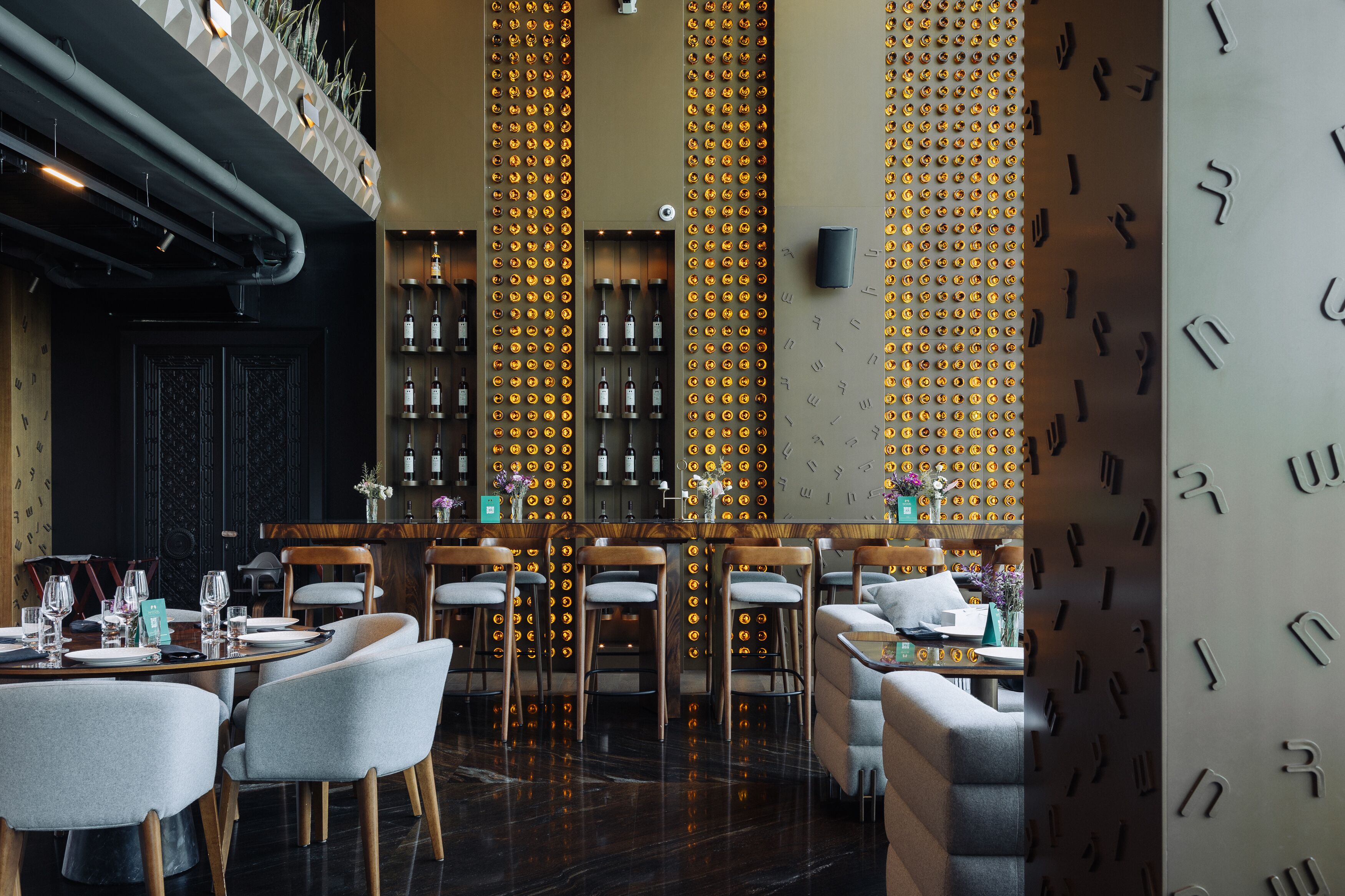 A restaurant with a bar area, wooden chairs, and a patterned wall.