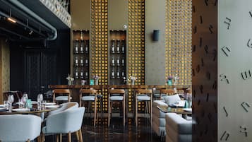 A restaurant with a bar area, wooden chairs, and a patterned wall.
