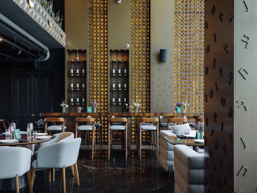 A restaurant with a bar area, wooden chairs, and a patterned wall.