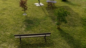 A grassy outdoor area with a picnic table, a bench, and a large umbrella.