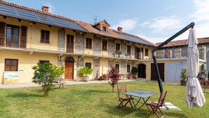 A courtyard with a dining table and chairs, a small tree, and a building with a tiled roof and balconies.