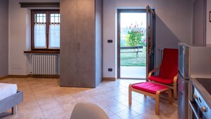 A modern room with a bed, a red chair, a kitchen area, and a sliding door leading to an outdoor area.