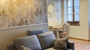 Ein modernes Wohnzimmer mit grauem Sofa, strukturiertem Wandpapier und einem Essbereich mit Holztisch und -stühlen.