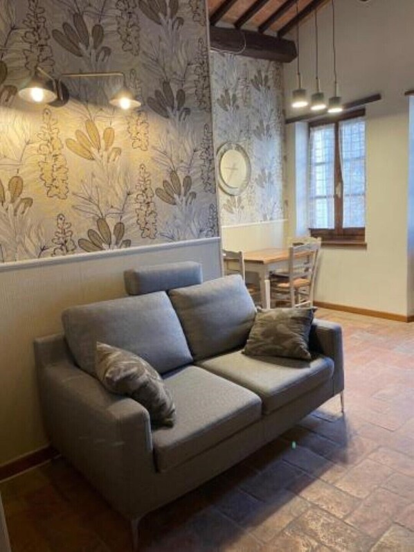 A modern living room with a grey sofa, patterned wallpaper, and a dining area with a wooden table and chairs.